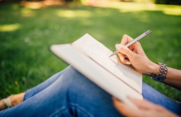 Woman sitting on grass writing in notebook.